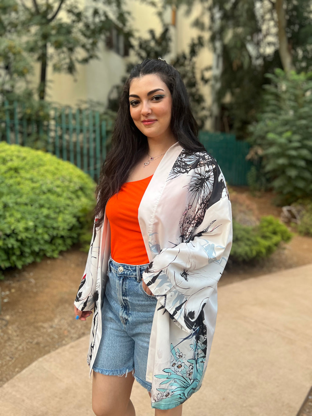 Woman wearing an orange top and denim shorts with a patterned kimono in an outdoor setting