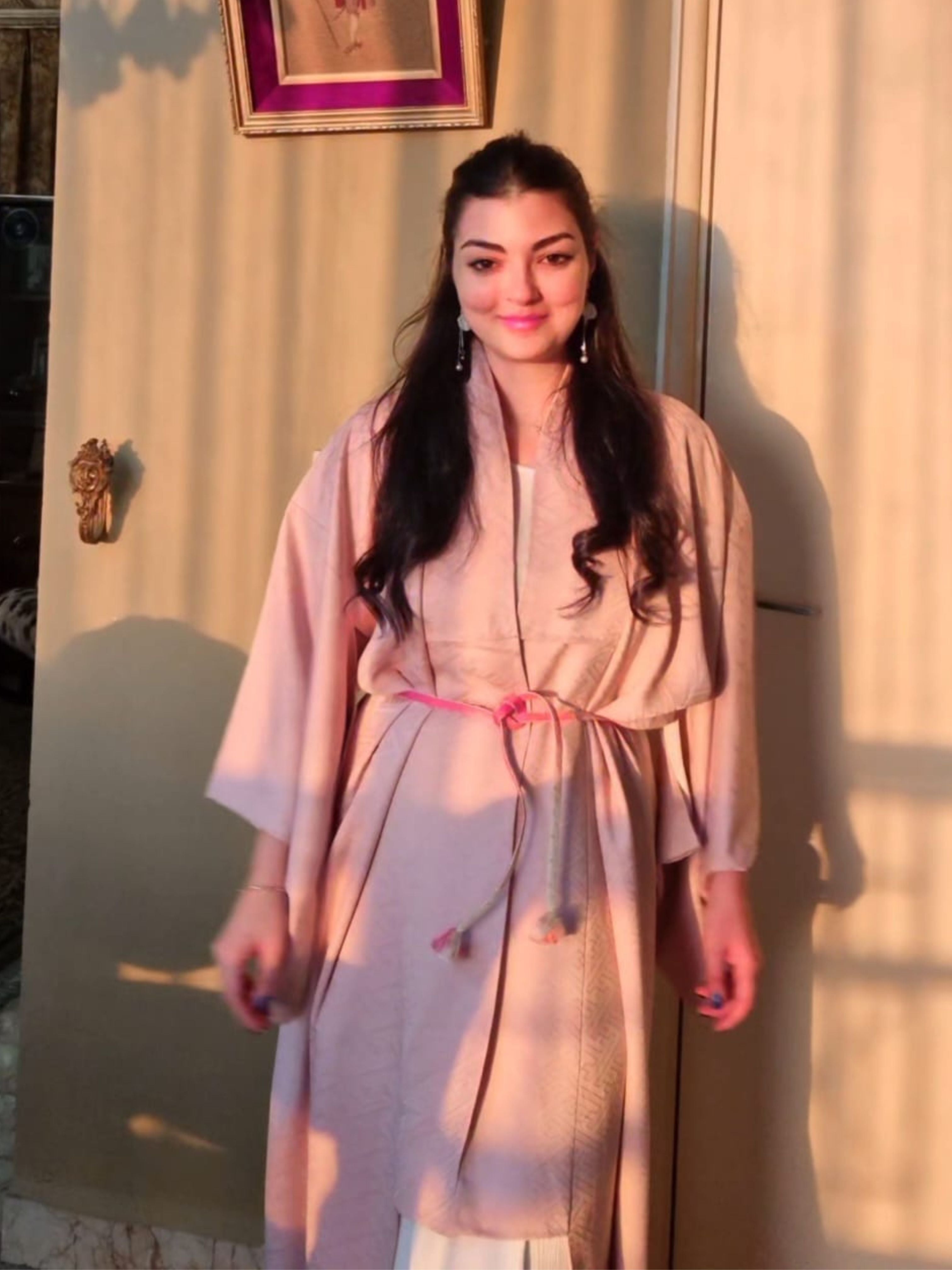 Woman in a light pink traditional Japanese kimono standing against a beige curtain.