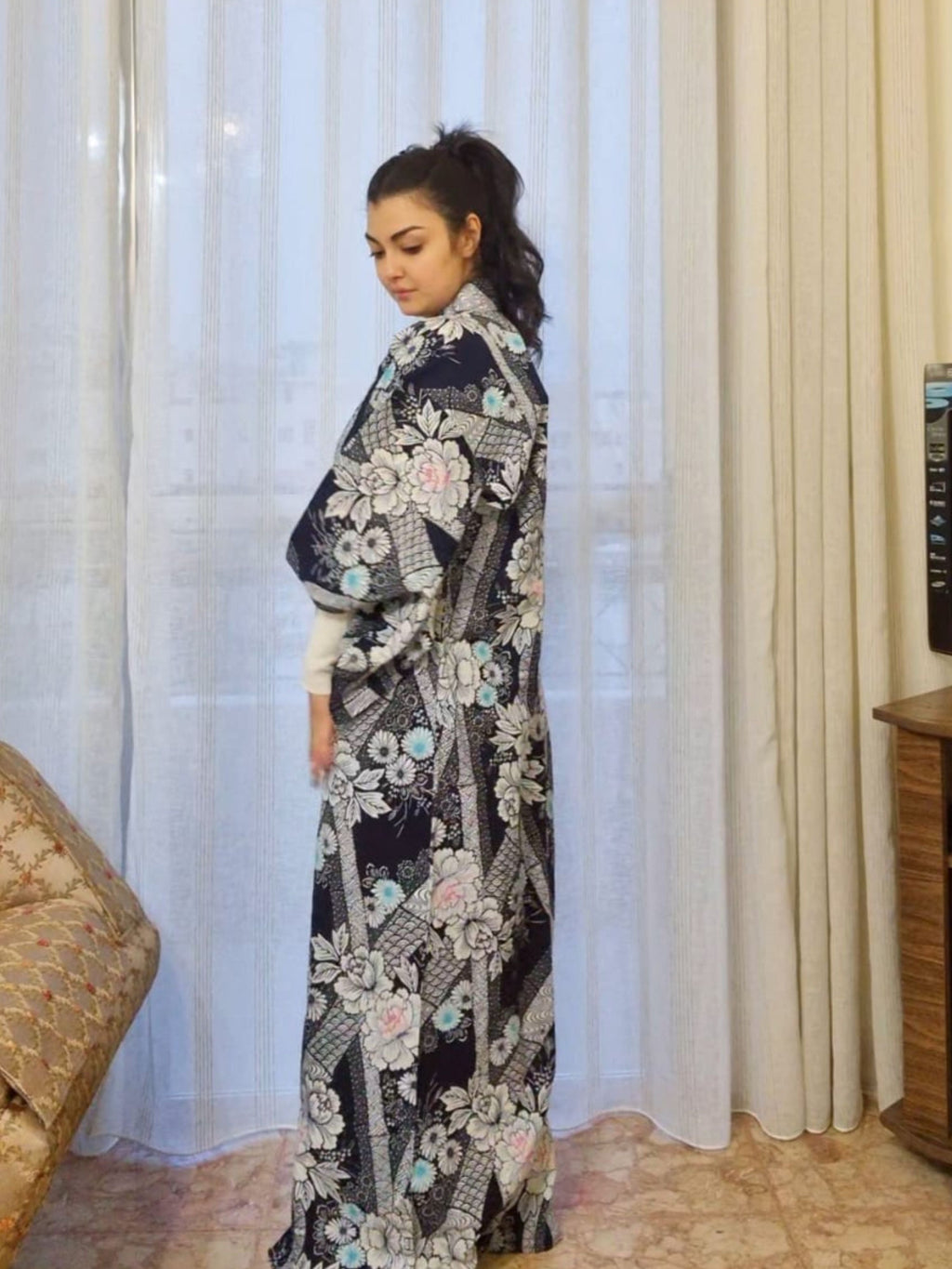 Woman wearing a floral embroidered kimono standing in front of a curtain.