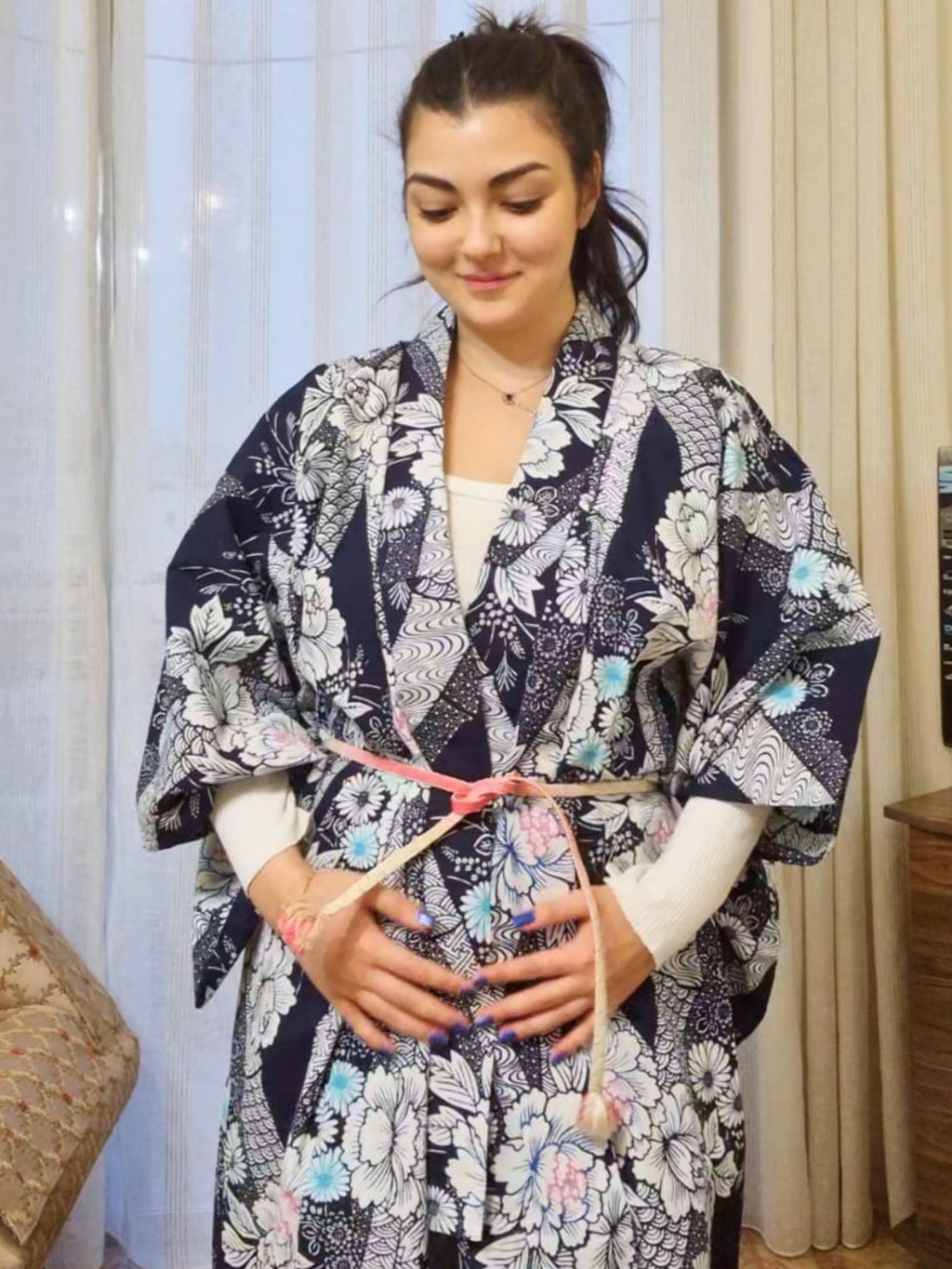 Woman wearing a floral kimono standing indoors with curtains in the background