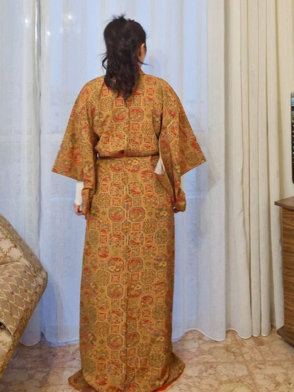 Person wearing a patterned kimono standing in front of white curtains.