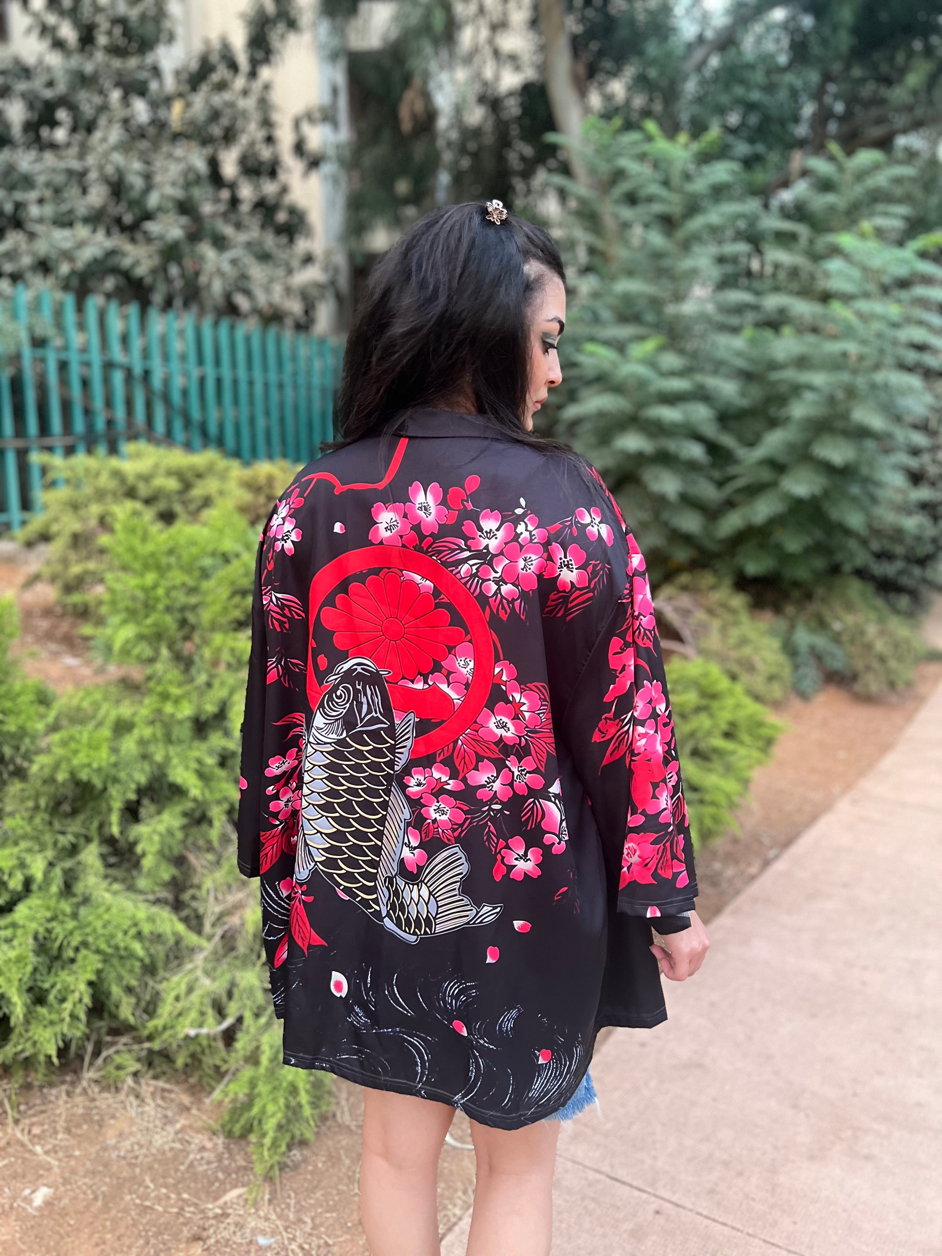 Woman wearing a black kimono with red and pink floral patterns and a large fish design, walking outdoors.