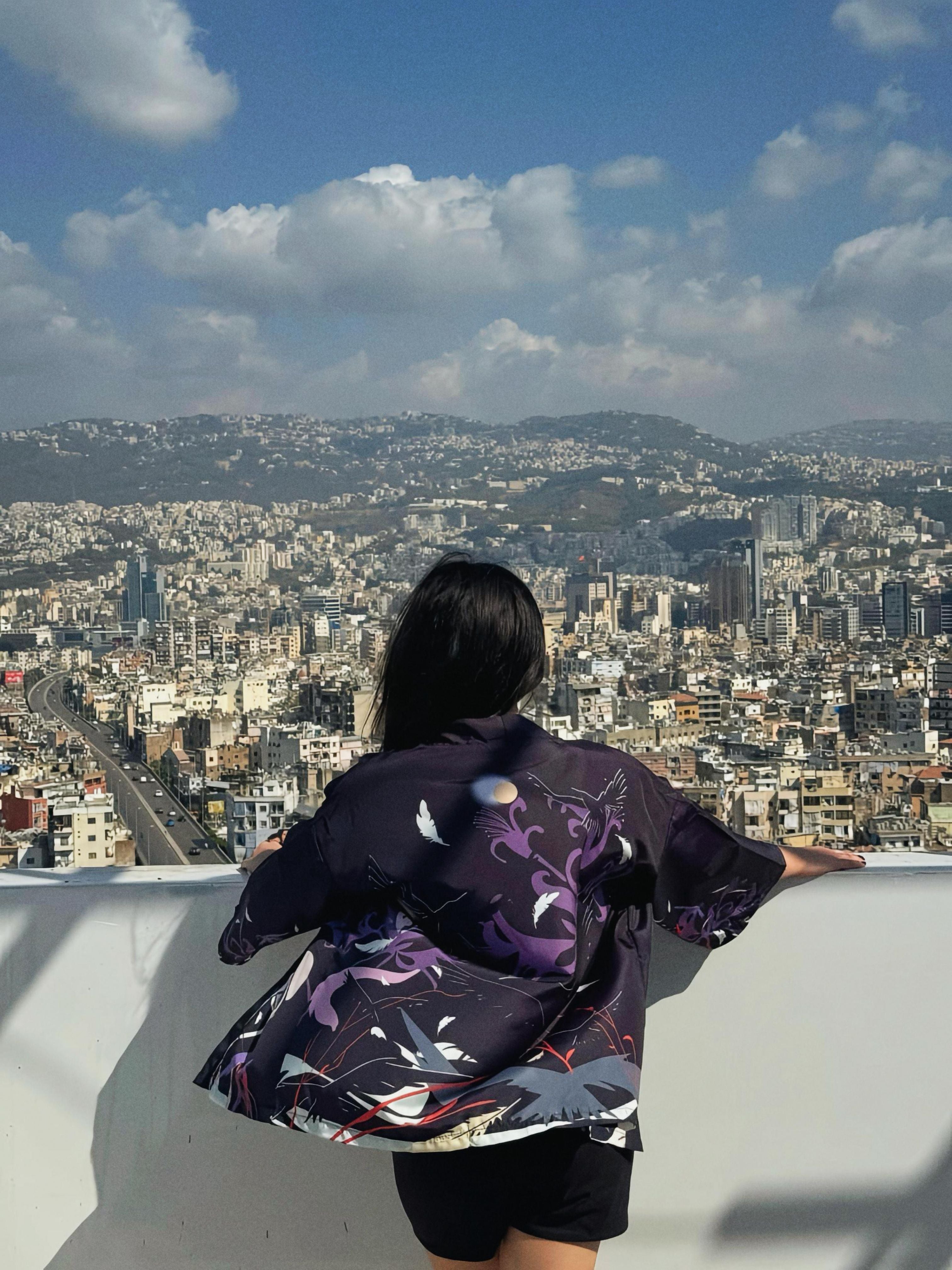 Person wearing a colorful jacket overlooking a cityscape with mountains in the background