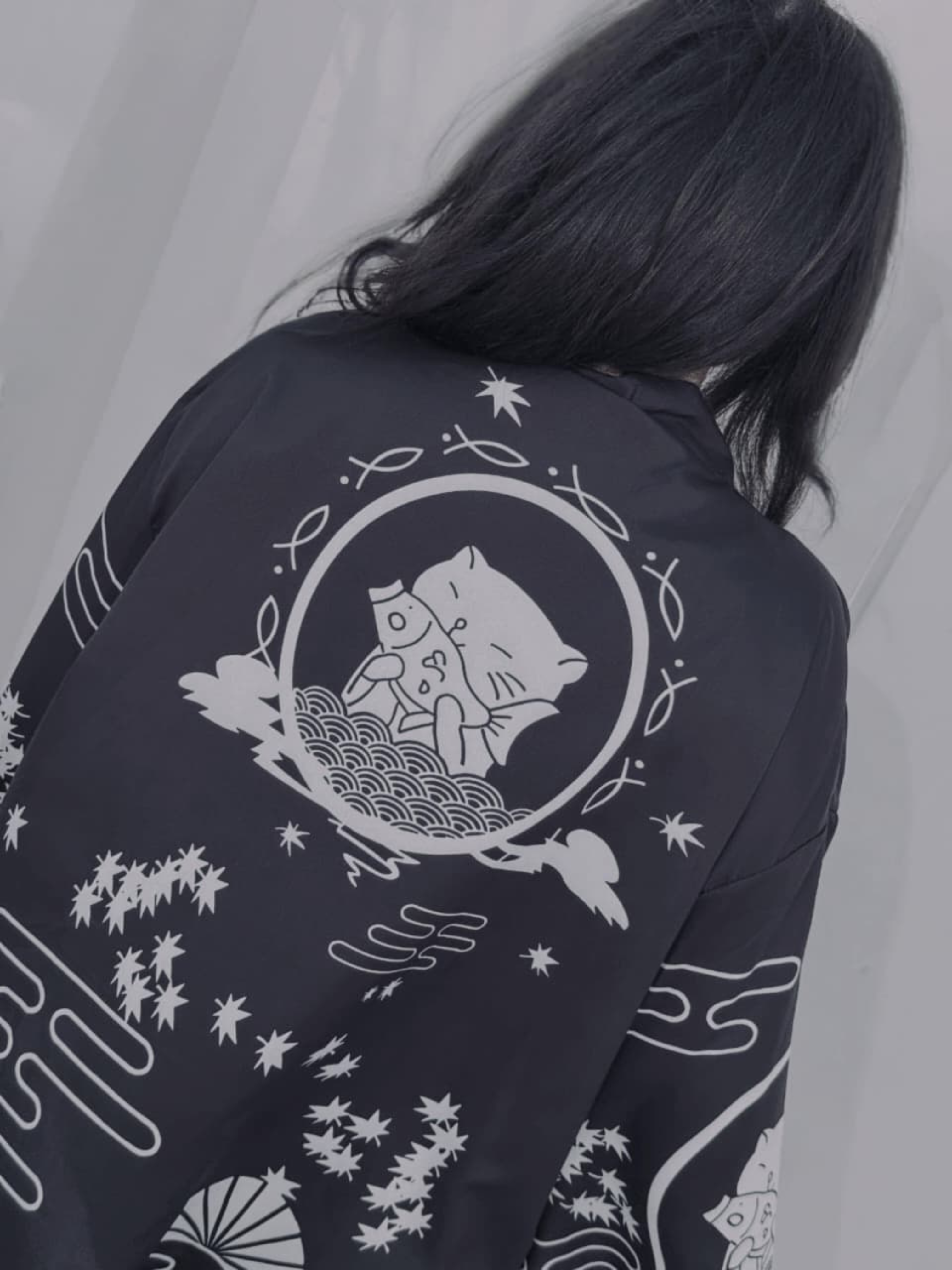 Person wearing a black jacket with white patterns and designs on the back