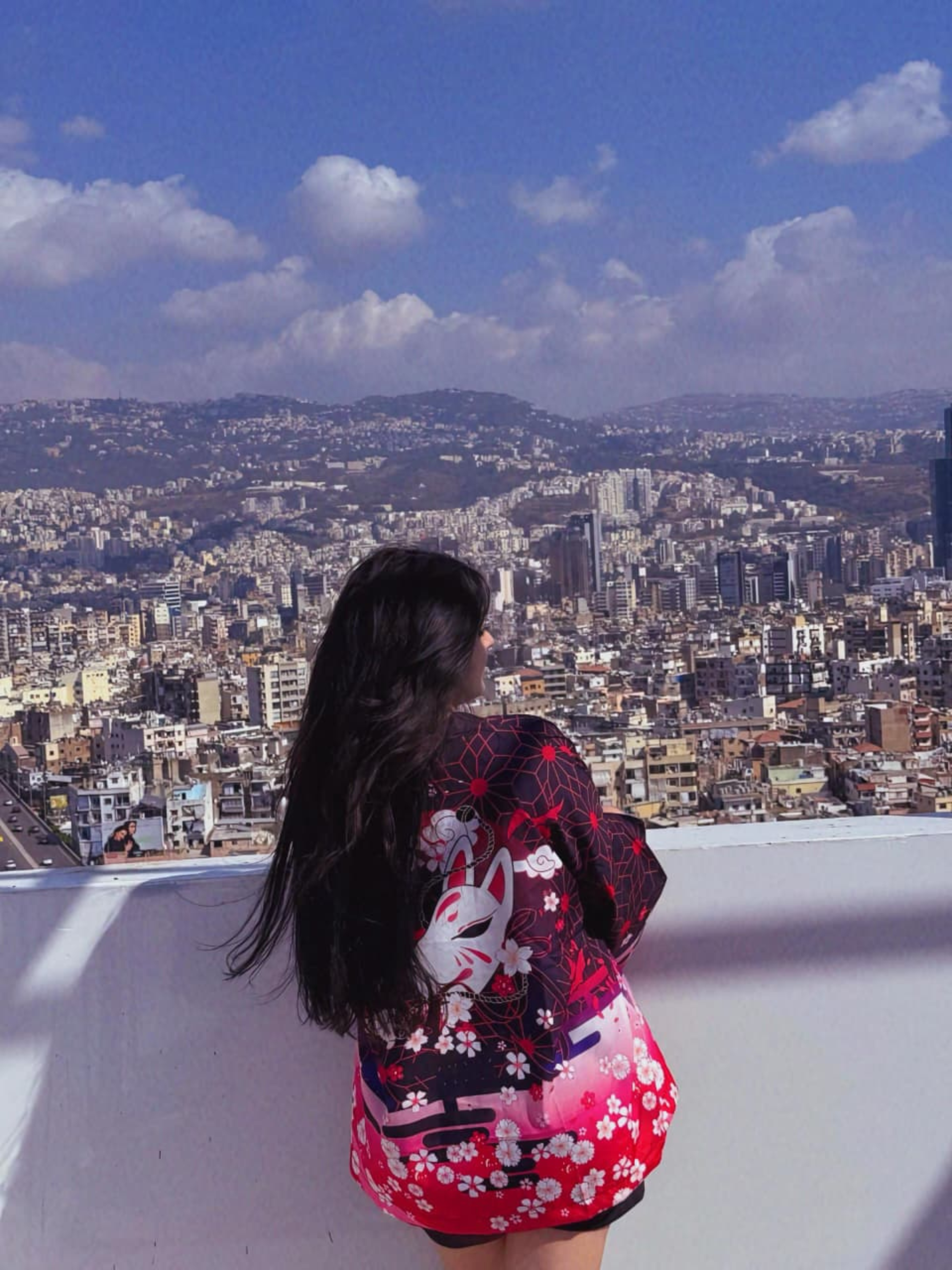 Woman in a colorful kimono overlooking a cityscape with a blue sky.