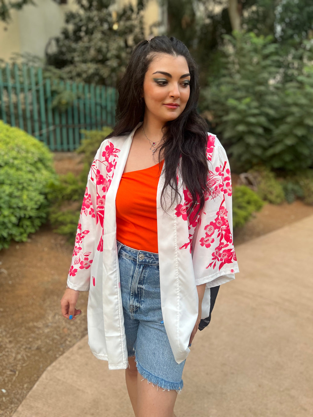 Woman wearing a white floral kimono over an orange top and denim shorts outdoors.